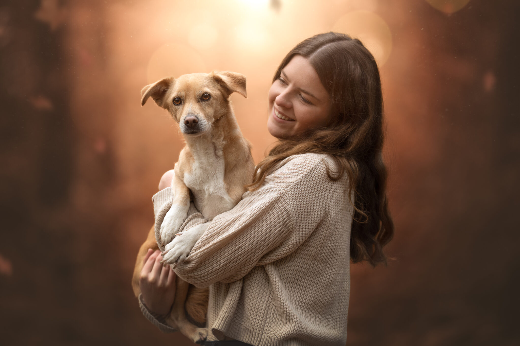 Junge Frau beim Tiershooting, hält Hund, draußen, Lächeln, warmes Licht, Hundefotograf.