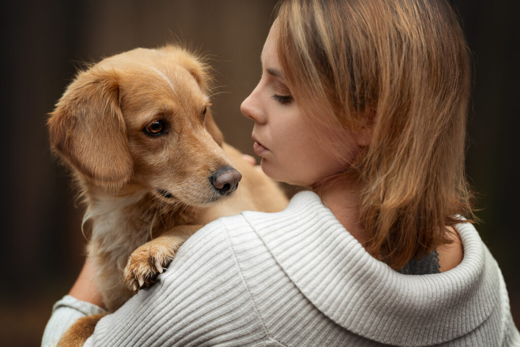 Tierfotograf Tiershooting: Frau mit braunem Hund, inniger Moment, dunkler Hintergrund.