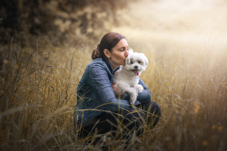 Frau im Feld, Tiershooting: Denimjacke, Hundekuss, goldenes Gras umgeben.