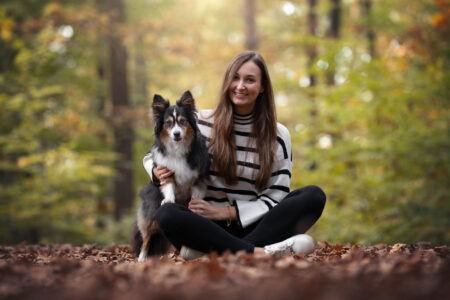Tierfotograf: Frau umarmt Hund beim Tiershooting, lächelt im Wald auf Laub.