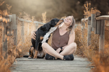 Tierfotograf, Tiershooting, Frau mit Hund auf einem sonnigen Steg, warme Atmosphäre.